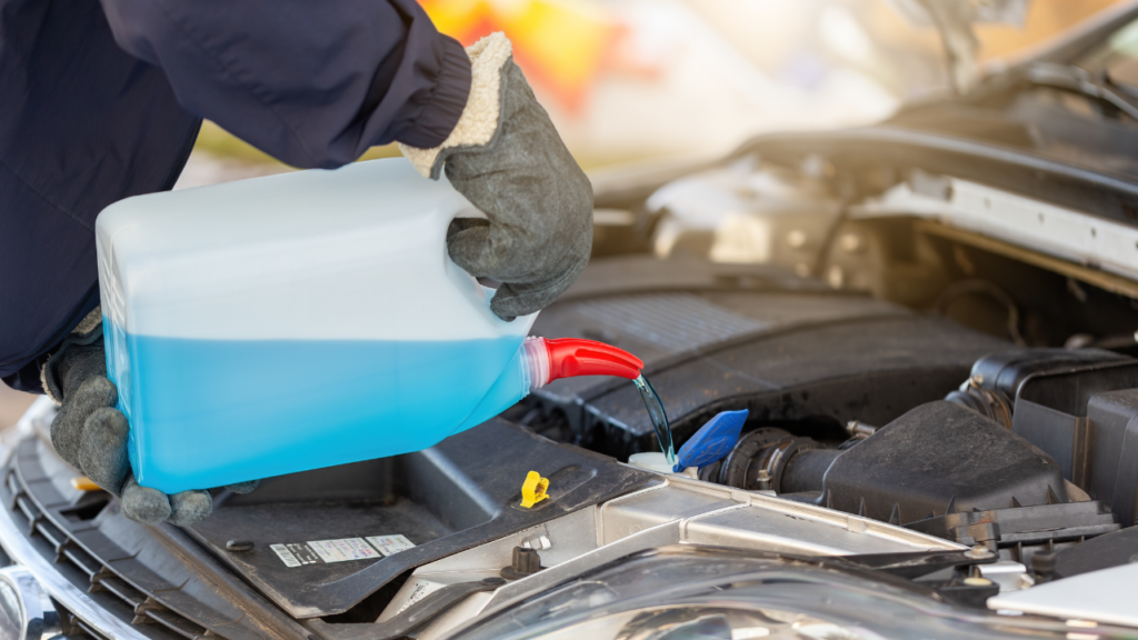 A car mechanic filling up a care with a blue window washer liquid