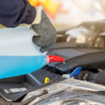 A car mechanic filling up a care with a blue window washer liquid