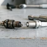 Worn spark plug next to a new spark plug and a spark plug socket